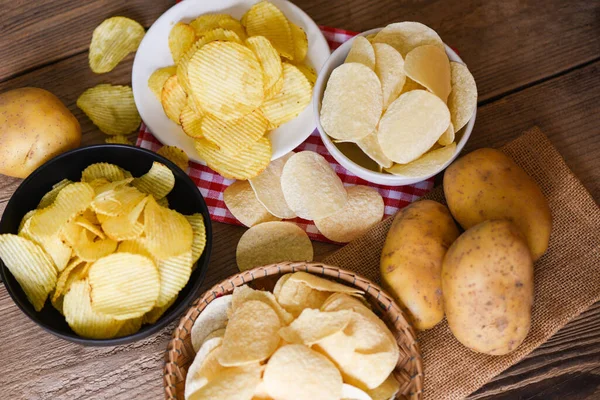 Potato chips snack on bowl and plate, Crispy potato chips on the kitchen table and fresh raw potatoes on wooden background - top view