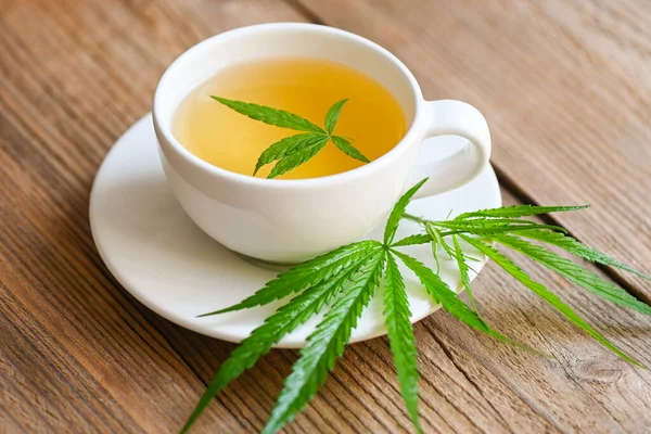 Cannabis tea herbal on tea cup with cannabis leaf marijuana leaves herb on wooden background, health tea with hemp leaf plant THC CBD herbs food and medical concept