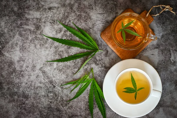 Cannabis tea herbal on tea cup with cannabis leaf marijuana leaves herb on dark background, health tea with hemp leaf plant THC CBD herbs food and medical - top view