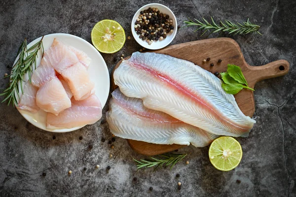 fish fillet on wooden board with ingredients for cooking, fresh raw pangasius fish fillet with herb and spices black pepper lemon lime, meat dolly fish tilapia striped catfish - top view