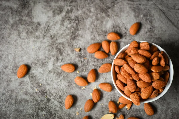 Almonds nuts on white bowl, Delicious sweet almonds on the table dark background, roasted almond nut for healthy food and snack