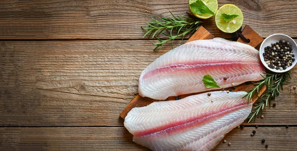 fresh raw pangasius fish fillet with herb and spices black pepper lemon lime, fish fillet on wooden board with ingredients for cooking, meat dolly fish tilapia striped catfish - top view