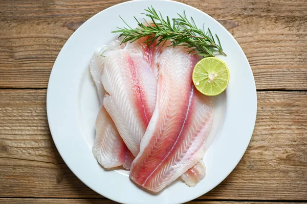 fresh raw pangasius fish fillet with herb and spices lemon lime and rosemary, meat dolly fish tilapia striped catfish, fish fillet on white plate with ingredients for cooking - top view