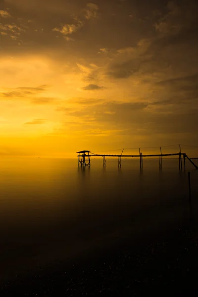A silhueta do velho molhe na praia durante o pôr do sol — Fotografia de Stock