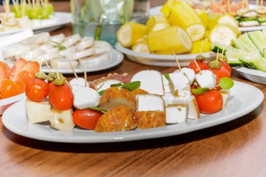 Peynir, kırmızı domates ve yeşil bezelye, şişlenmiş, tabakta istiflenmiş.