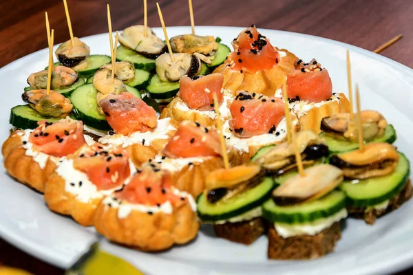 Kırmızı balıklı sandviç susam tohumları serpiştirilmiş ve patlıcanlı salatalıklar bir tabağa serpilmiş.