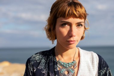 Genç, sarışın, güzel bir kadın. Kumsaldaki kameraya bakıyor.