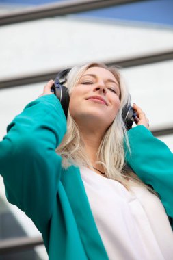 Genç sarışın bir kadın, kulaklıklarla müzik dinliyor ve eğleniyor.