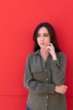 Genç esmer kadın, kırmızı arka planda yeşil bir gömlek giyiyor.