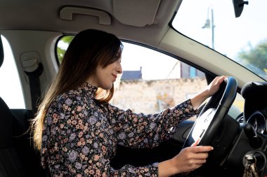 Kendinden emin ve mutlu genç esmer kadın araba kullanıyor.