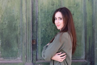 Genç, esmer, şık bir bayan yeşil eski bir kapı arkasında poz veriyor.