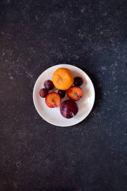 Gri bir arka planda çiğ erikler ve üzümler.