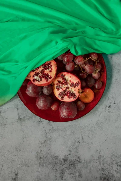 Plums, pomegranate and grapes covered in green in a grey stone background — Stok fotoğraf