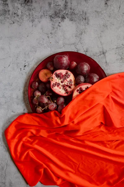Çiğ erikler, nar ve üzümler, gri bir arkaplanda kırmızıyla kaplanmış. — Stok fotoğraf