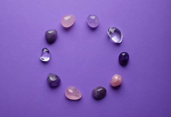 The circle is lined with natural minerals. Semi-precious stones of different colors processed. Amethyst and rose quartz. Frame of gems on purple background.