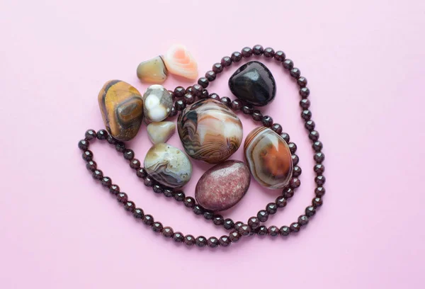 Garnet beads and round agate bostwan stones on pink background. Multicolored gemstones, tumbled minerals.