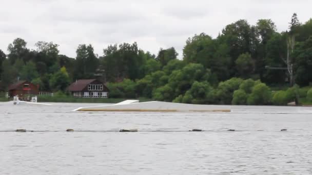 A man in a helmet rides a wakeboard in a wake park. jumping over obstacles on the water. active sports — Video