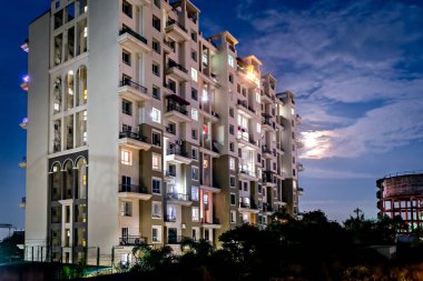 Ayın mavi gökyüzünde batışı, modern, aydınlık bir binanın arkasında geceleri..