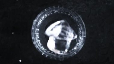 Süper Yavaş Çekim Buz Küpü Karanlık Arkaplanda Votka ile 1000 fps 'de bardağa düşüyor. 4K Çözünürlükte Yüksek Hız Sinema Kamerası ile Çekim.