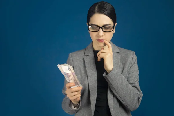 Krásná mladá žena v šedé bundě s ruskými rubovými penězi v rukách přemýšlela. modré pozadí — Stock fotografie
