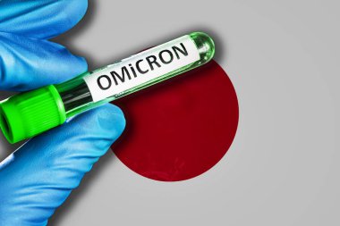 Japan outbreak of omicron variant. A hand in a blue rubber glove holds a test tube with covid-19 virus omicron in front of Japan flag. Omicron variant outbreak concept