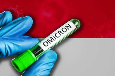 Monako salgını Omikron varyantı. Mavi lastik eldivenli bir el Monako bayrağının önünde üzerinde covid-19 virüsü olan bir tüp tutar. Omicron varyant salgını kavramı