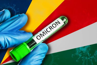 Seyşeller Omikron salgını. Mavi lastik eldivenli bir el, Seyşeller bayrağının önünde kovid 19 virüslü bir tüp tutuyor. Omicron varyant salgını kavramı