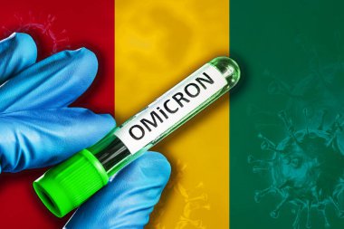 Omikron varyantı salgını. Mavi lastik eldivenli bir el Gine bayrağının önünde kovid 19 virüslü bir tüp tutuyor. Omicron varyant salgını kavramı