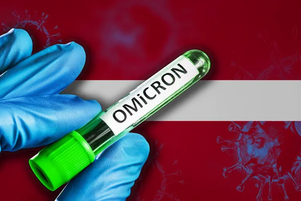 Letonya 'daki Omikron salgını. Mavi lastik eldivenli bir el Letonya bayrağının önünde üzerinde covid-19 virüsü olan bir tüp tutuyor. Omicron varyant salgını kavramı