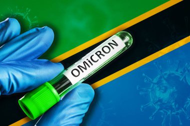Tanzanya salgını Omikron varyantı. Mavi lastik eldivenli bir el, Tanzanya bayrağının önünde kovid 19 virüslü bir tüp tutuyor. Omicron varyant salgını kavramı