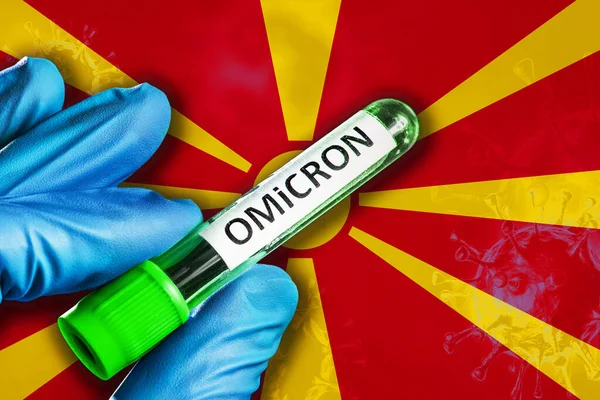 Ξέσπασμα της παραλλαγής όμικρον στη Βόρεια Μακεδονία. Το χέρι κρατά δοκιμαστικό σωλήνα με omicron του ιού covid-19 μπροστά από τη σημαία — Φωτογραφία Αρχείου