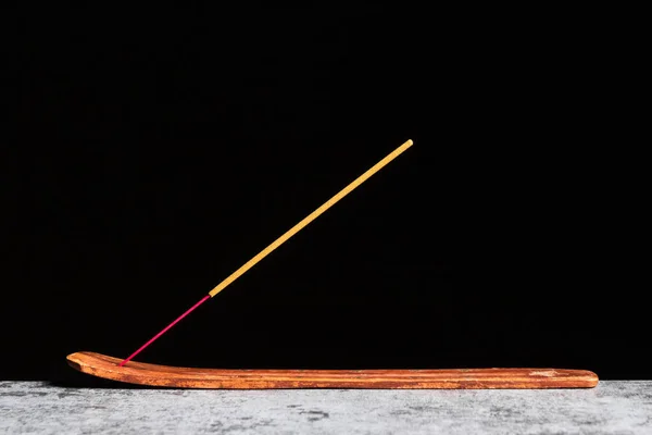 A stick of incense stands on a wooden stand insulated on a black background.