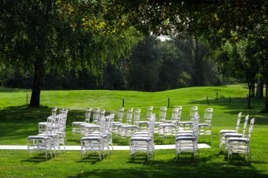 Yeşil çimenlikteki bir düğün töreninde şeffaf plastik sandalyeler. Boşluğu kopyala