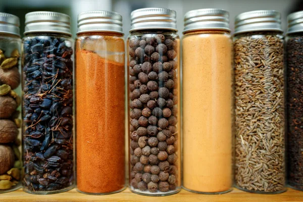 Dried barberry, ginger and cumin or zira and other spices in transparent jars among other spices on the table in home kitchen — Stock Photo, Image