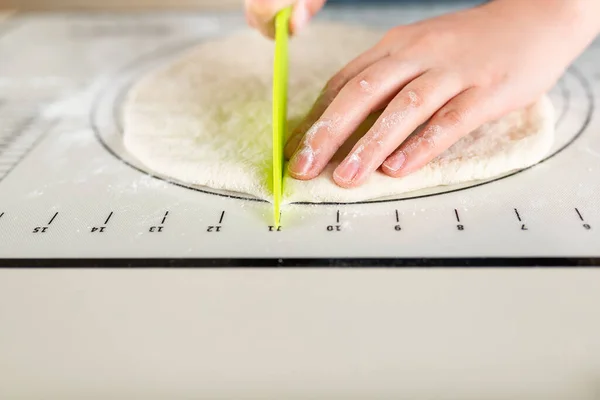 Cutting wheat dough on a baking mat with markings with a plastic knife, copy space.