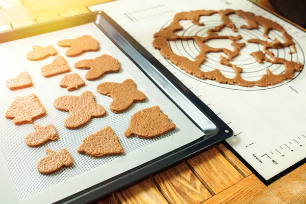 Christmas cookies laid out on a silicone baking mat on a baking sheet on a wooden table.