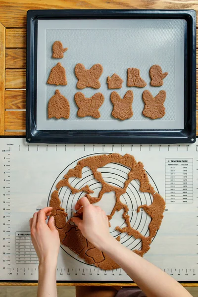 A woman prepares New Year's homemade cookies on a silicone baking mat. Top view, vertical.