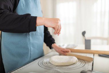 Önlüklü şef, buğday ekmeğine un serpiyor silikon hamurlu hasırın üzerine. Seçici odak, boşluğu kopyala.