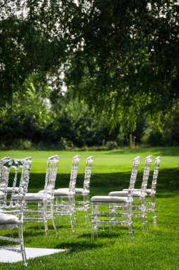 Yeşil çimenlikteki bir düğün töreninde şeffaf plastik sandalyeler. Uzayı kopyala, dikey.