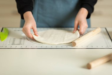 Mavi önlüklü bir aşçı, hamuru mutfak silikon fırın paspasından çıkarır. Ellerin ve çalışma alanının görüntüsü. Boşluğu kopyala.