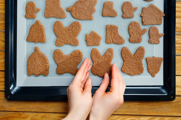 Top view of female hands spreading different shaped homemade cookies on a silicone baking mat on a baking sheet.