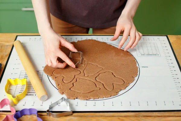 View of female hands squeezing out homemade cookies from rolled gingerbread dough with culinary molds.