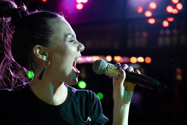 Jong zingen vrouw met microfoon het hebben van plezier op open podium in karaoke club — Stockfoto