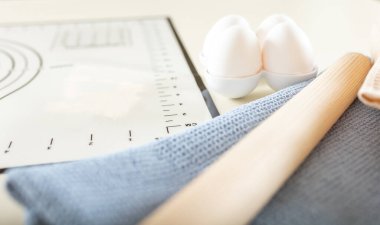 Yumurtaların, mutfak havlusunun, oklavanın ve silikon fırın paspasının olduğu mutfak masasına yakın plan. Her şey pişmeye hazır.