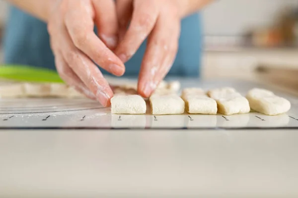 Close-up of floured hands spreading even pieces of dough along the markings on a kitchen baking mat