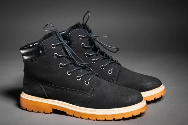 A pair of black winter mens boots with laces and a light sole on a gray background, side view — Stockfoto