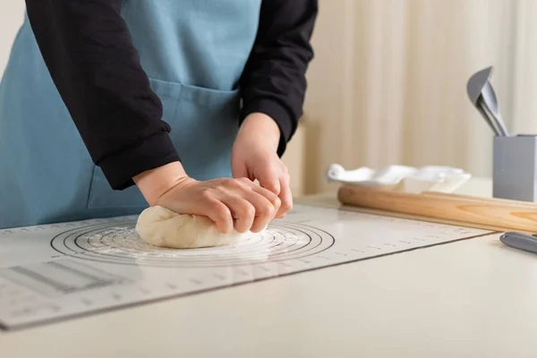 The hands of the cook knead the wheat dough on a rubber kitchen mat with different markings for ease of use