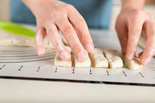 Close-up of floured hands spreading pieces of dough along the markings on a silicone baking mat