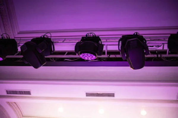 Professional lighting equipment beam and fill hanging on a truss above the ceiling in concert hall.