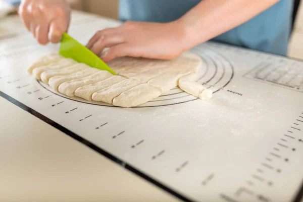 Side view on cutting wheat dough on a baking mat with markings with a plastic knife on the kitchen table, copy space.
